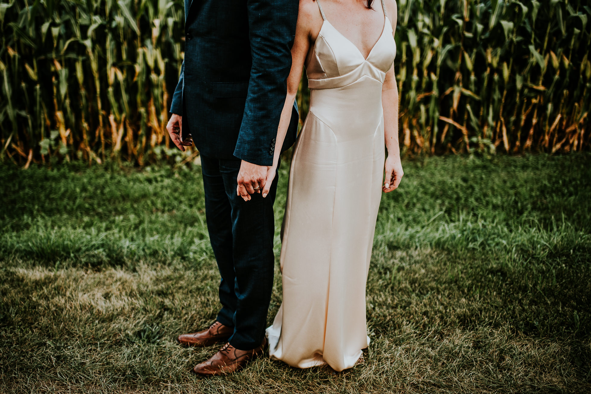bride and groom holding hands near corn field at olde tater barn wedding in central bridge, ny photographed by traverse the tides