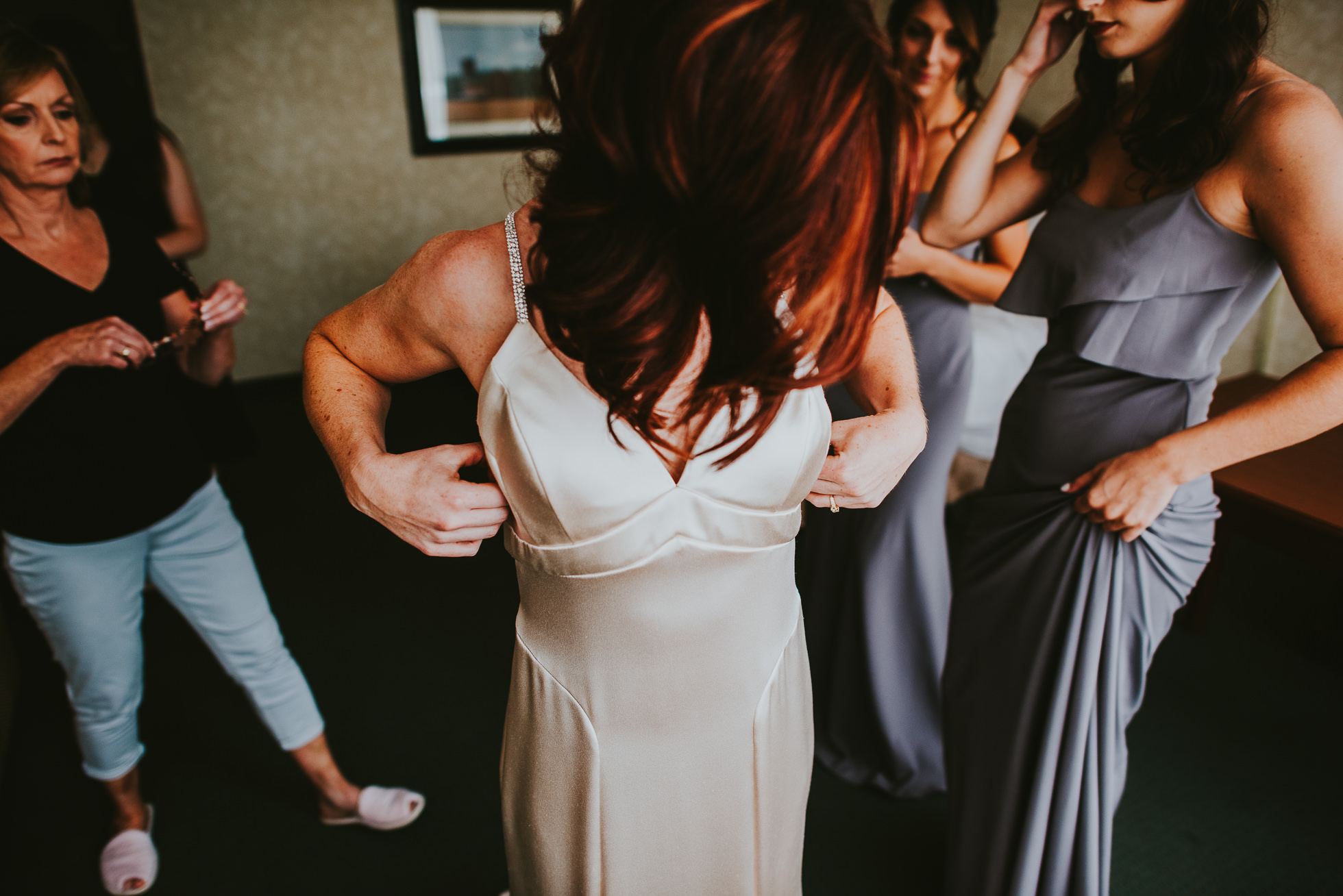 bride getting dressed with mom and bridesmaids at olde tater barn wedding in central bridge, ny photographed by traverse the tides