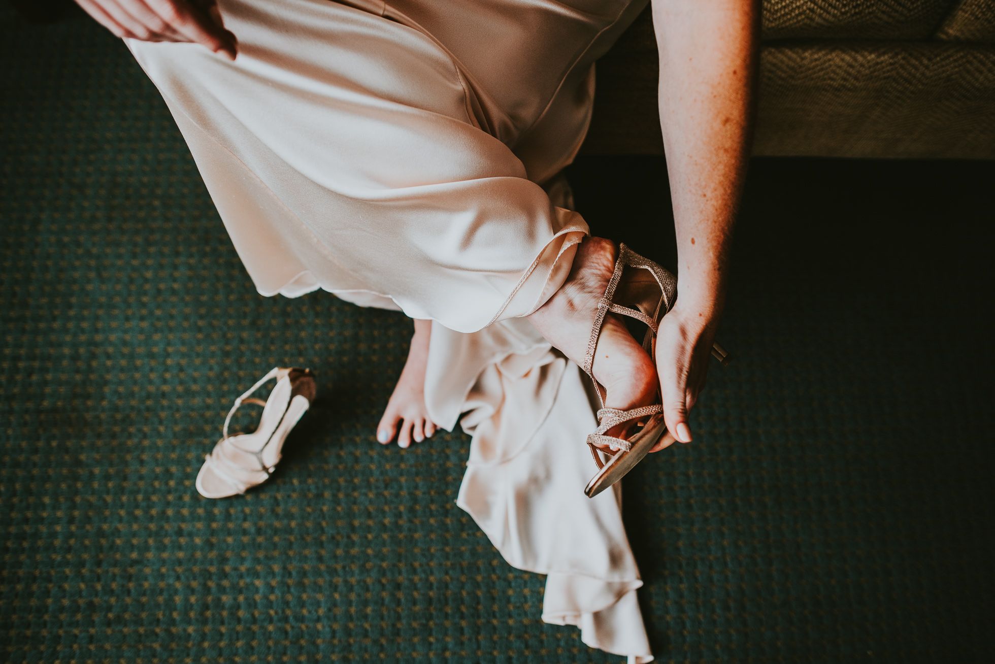 bride putting wedding shoes on at olde tater barn wedding in central bridge, ny photographed by traverse the tides