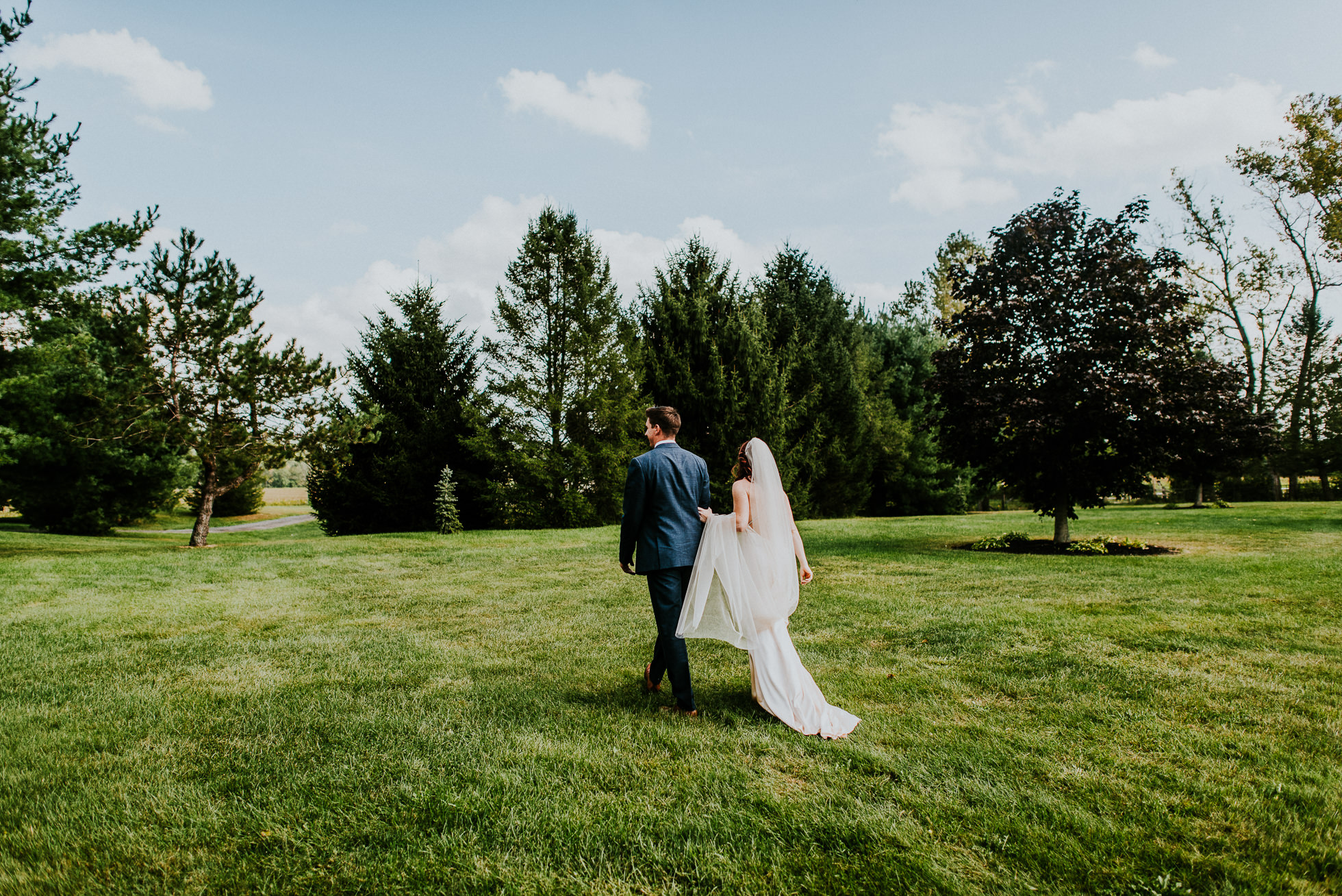 bride and groom walking through open field at olde tater barn wedding in central bridge, ny photographed by traverse the tides
