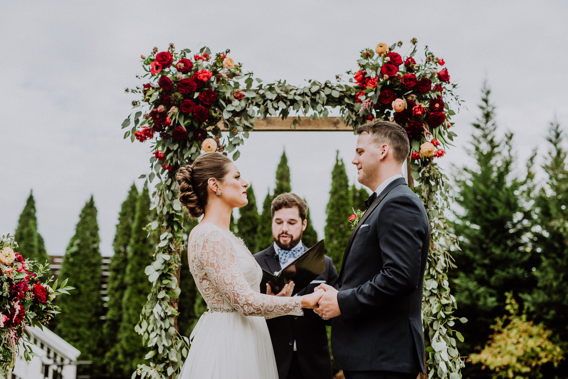 bride and groom holding hands in front of floral arch the cordelle nashville wedding