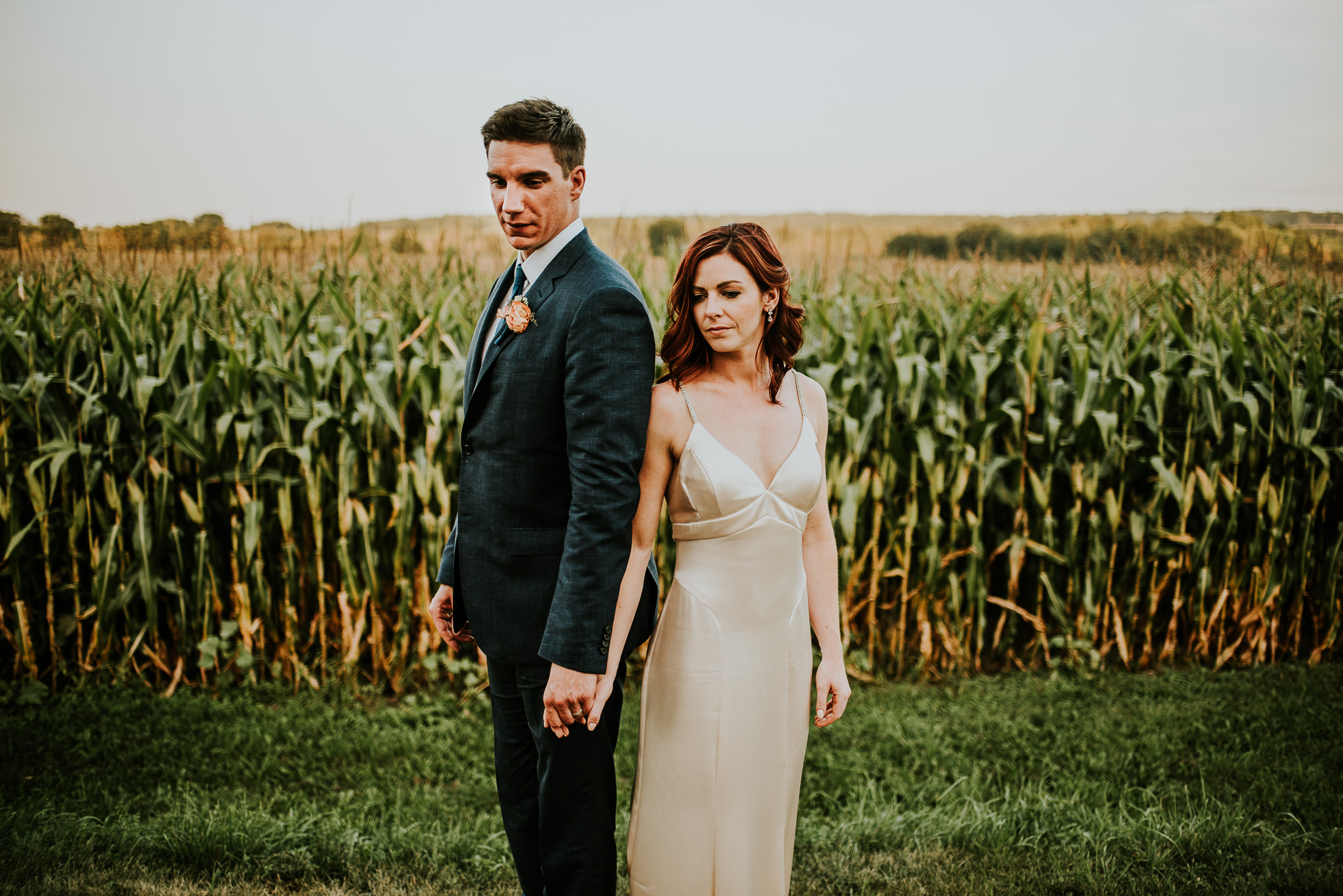 bride and groom holding hands near corn field at olde tater barn wedding in central bridge, ny photographed by traverse the tides